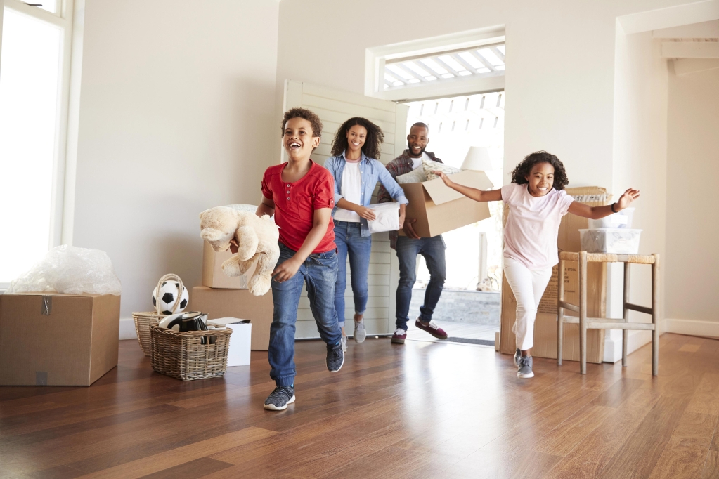 Excited Family Carrying Boxes Into New Home On Moving Day Excited Family Carrying Boxes Into New Home On Moving Day